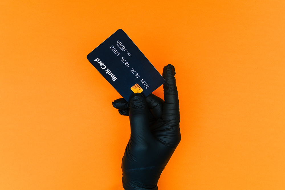 A hand wearing a black disposable glove holds a credit card.