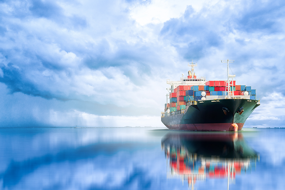 A container ship sails on the ocean with a cloudy sky.