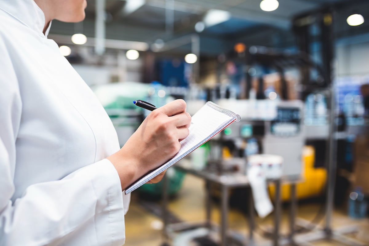 A person holds a clipboard with a factory in the background.