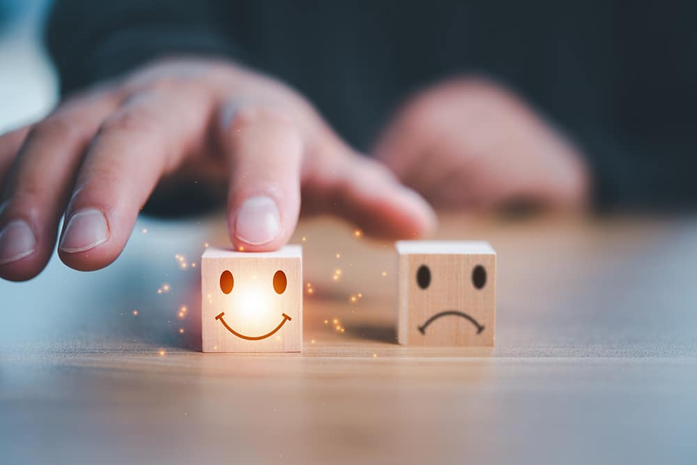 Smiley face and unhappy face wood blocks sit on a table, with the former illuminated.